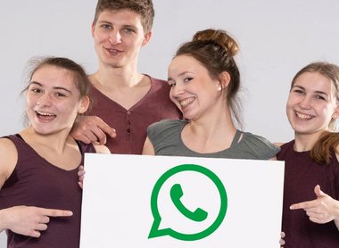 Eine Gruppe von jungen Menschen, die sich freuen und ein Schild mit dem WhatsApp-Logo hochhalten.